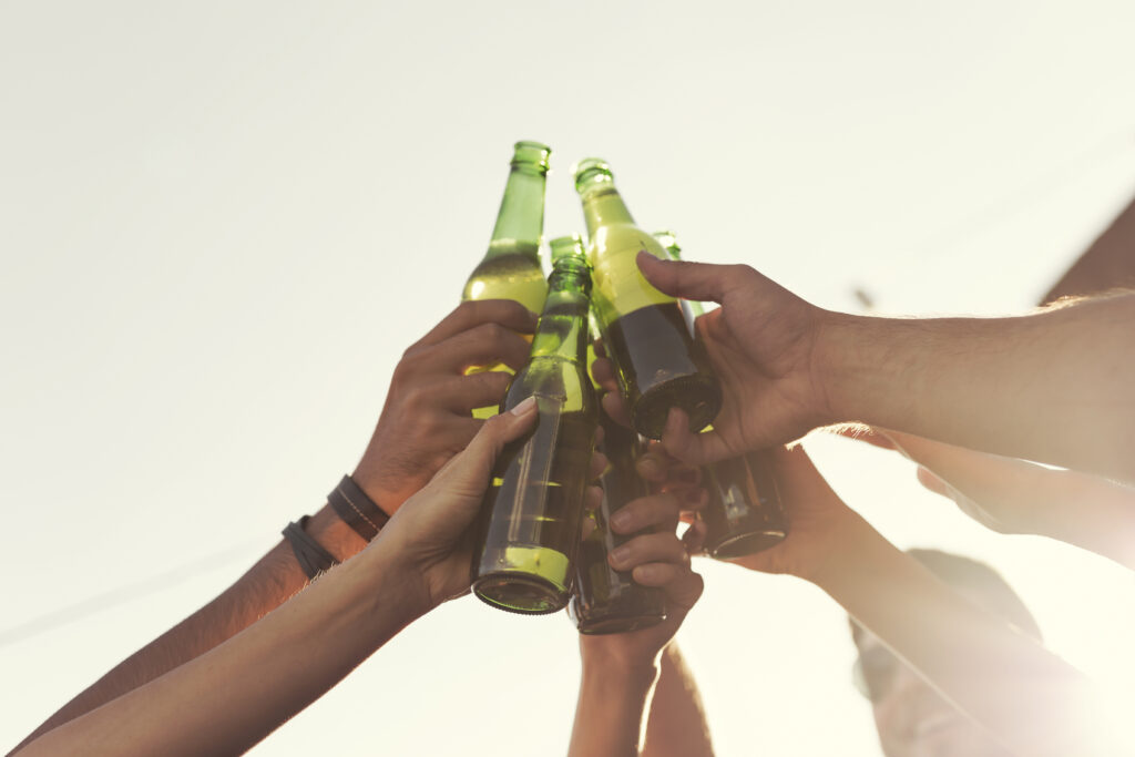 Detail of hands holding beer bottles, making a toast and enjoying hot summer days. Selective focus on the female hand on the left